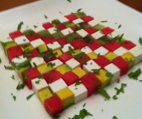 מנה הכוללת תבנית דמקה עשויה מקוביות קטנות של מרכיבים שונים, ככל הנראה כולל אבטיח, גבינת פטה, אבוקדו ומנגו. את הקוביות מסדרים בצורה מסודרת על צלחת לבנה, מעוטרים בעשבי תיבול קצוצים.