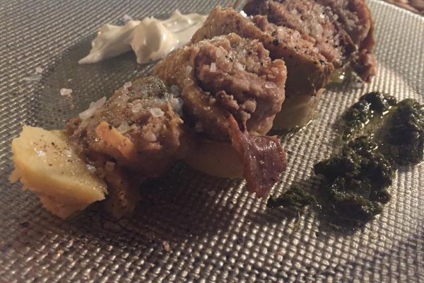 צלחת עם לחמניות בשר ממולאות פרוסות מעוטרות במלח. לצד הבשר יש כדורי שמנת ורוטב עשבים ירוקים. האוכל מוגש על צלחת זכוכית בעלת מרקם שקופה.