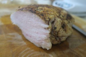 תקריב של חתיכת בשר מבושלת, כנראה עוף או הודו, עם חיצוניות שחומה ופנים בהיר. היא מונחת על קרש חיתוך מעץ ושתין נראית בחלקה בצד הימין.