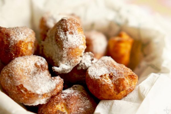 תמונת תקריב של כמה סופגניות אבקת סוכר מסודרות על משטח מרופד בנייר. הסופגניות חומות-זהובות עם אבק קל של סוכר לבן, המדגיש את משטחי המרקם שלהן.