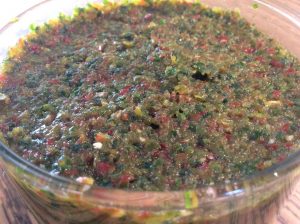 תקריב של קערה מלאה בסלסה קצוצה דק. השילוב כולל שנים ירוקים ואדראים לעין, המרמזים על עשבי תיבול ופלפלים, המפוזרים באופן שווה על פני שטח הקערה ומרמזים על מרקם גס ומעורבב.