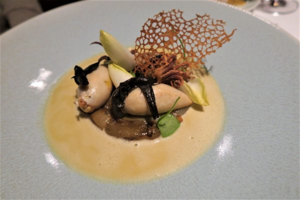 מנת גורמה בצלחת כוללת שני פריטים ממולאים בציפוי אצות, מונחים על פטריות מוקפצות. הוא מעוטר באנדיב וסריג עדין ופריך, מוקף ברוטב שמנת.