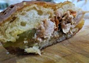 תקריב של חתך כריך על משטח עץ. הכריך מכיל עוף מגורר, חמוצים ירוקים גלויים ורוטב חום. הלחם נראה רך ומעט שחום.