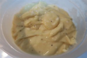 קערה לבנה המכילה מיונז צהוב שמנת עם כתמי פלפל שחור גלויים. למיונז מרקם סמיך וחלק.