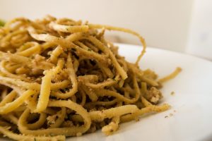 תקריב של צלחת ספגטי מצופה ברוטב בהיר, מעוטר בפיסות קטנות של עשבי תיבול ופירורים. הפסטה מסודרת בצורה סתמית, מעט מבולגנת על הצלחת הלבנה.