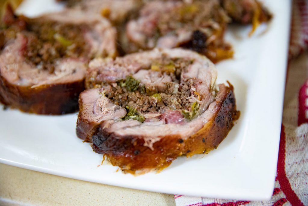 פרוסות גליל בשר ממולא עם חיצוניות שחומות ומילוי של בשר טחון וירקות ירוקים מסודרות על צלחת מלבנית לבנה. בד אדום ולבן נראה חלקית ליד הצלחת.