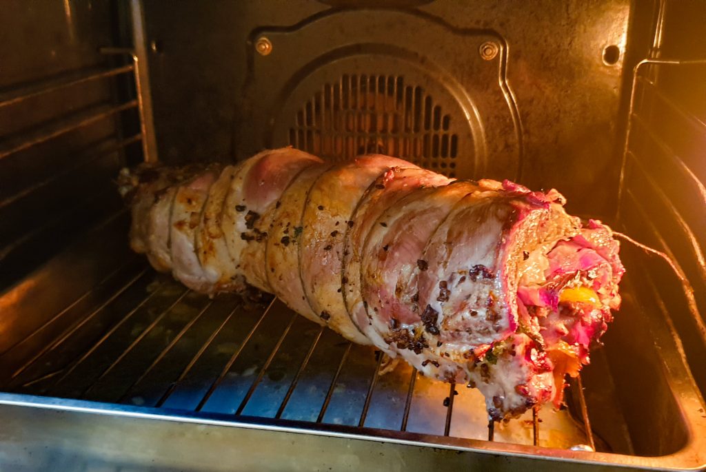 צלי בשר מגולגל וממולא מתבשל על מתלה בתוך תנור. הבשר קשור בחוט וחלקו החיצוני חום-זהוב. הפנים גלוי עם קצת מלית, כולל ירקות. נורית התנור דולקת, מאירה את הצלי.