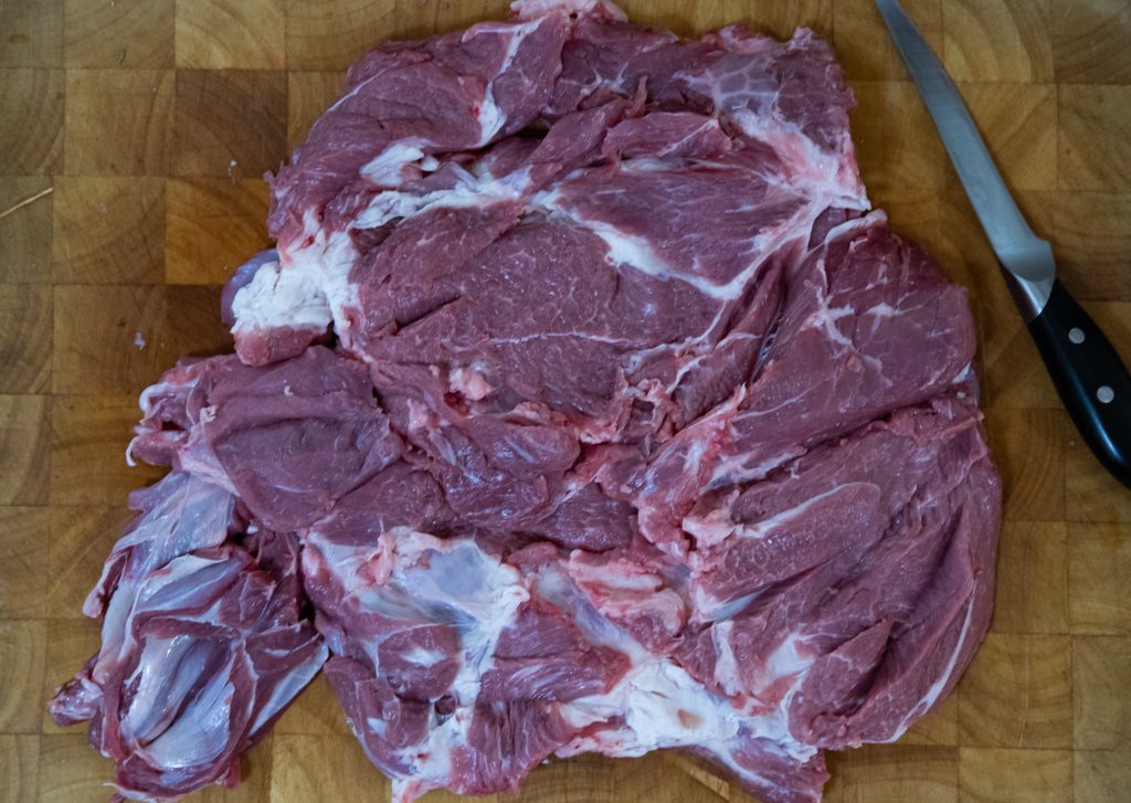 ממרח של נתחי בשר נאים ולא מבושלים מונחת על משטח עץ. מימין לבשר מניחים סכין עם ידית שחורה. נראה שלבשר יש מרקמים ועוביים משתנים.