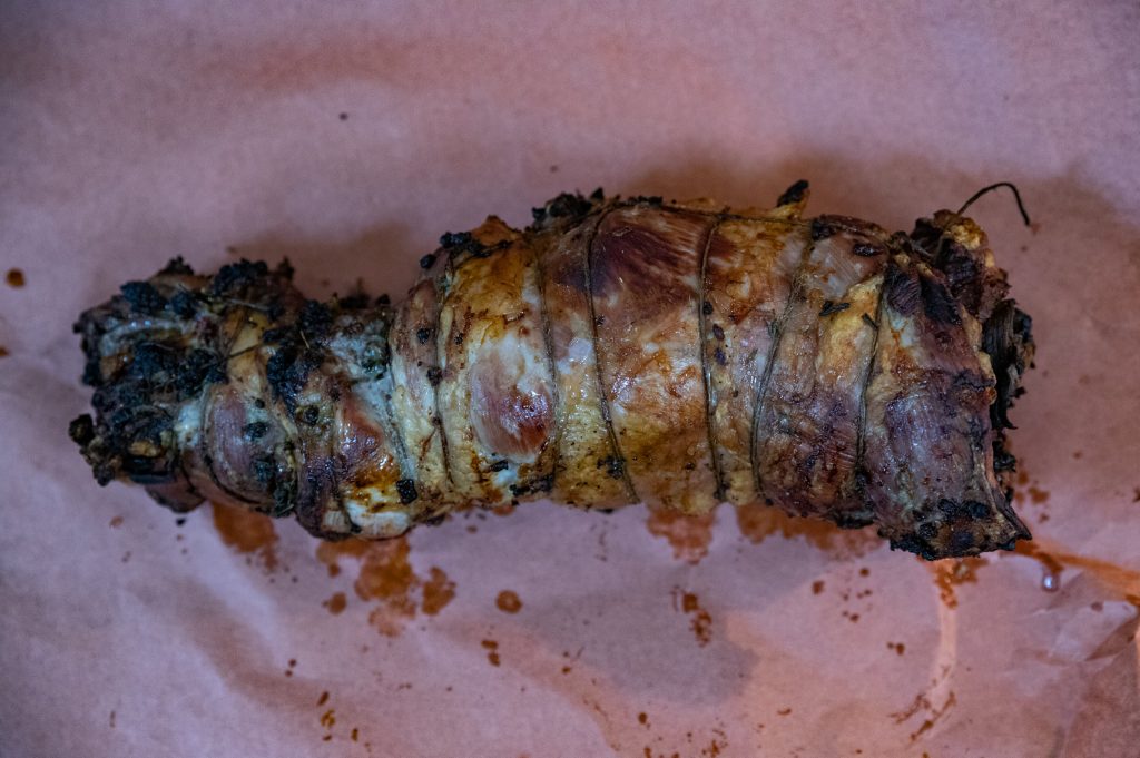 רולדה מבושלת, קשורה בחוט, מונחת על דף נייר פרגמנט. הבשר נראה שחום עם כמה אזורים חרוכים, ועשבי תיבול נראים לאורך הקצוות. ניתן לראות מיצים על הקלף המקיף את הרולדה.