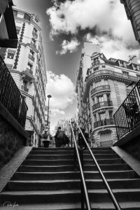 תמונה בשחור-לבן של גרם מדרגות אבן המוביל כלפי מעלה בין שני בניינים מעוטרים עם מרפסות. שלושה אנשים נראים למעלה. שמים מעוננים ברקע. מסילות עוברות במרכז ובצידי המדרגות.