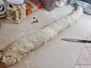 גילגול ארוך ולא אפוי, מונח על משטח המטבח. סכין מוצרים שונים למטבח, כולל צנצנת שום מזון ושקיות, נמצא בקרבת מקום.